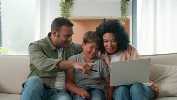 快乐的家庭小男孩与父母一起在沙发网上购物 父母用银行卡在笔记本电脑上教儿子购买家居用品 — 图库视频影像