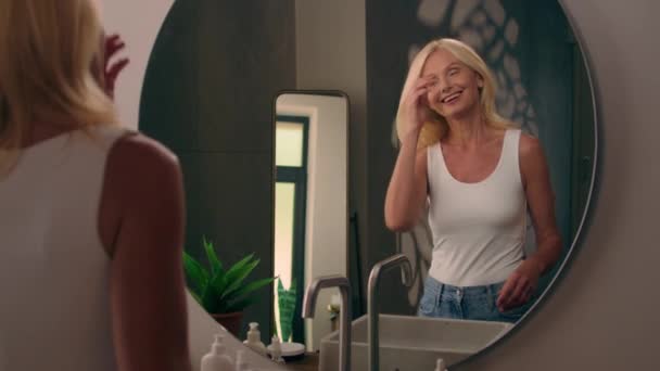 美しい白人中年の成熟した女性は ホームトイレに行きます 笑顔を見る ミラー美容ルーチンメイクアップヘアケア スタイリッシュなヘアカット高級シャンプー修理バーム光沢反老化栄養化粧品 — ストック動画