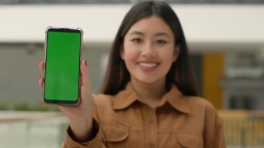 Cep telefonu cihazı odaklı bulanık Asyalı iş kadını Çinli kız akıllı telefon tutuyor yeşil model mutlu iş kadını cep telefonu krom anahtar boş web servis aygıtı reklamı yapıyor