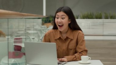 Mutlu Asyalı sürpriz Koreli iş kadını kafeterya birincisi kadın online dizüstü bilgisayarda ödül kazanıyor iş başarısını kutluyor zafer çığlığı, internet sitesi reklamında parmak işareti.