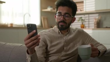 Arap erkek, etnik erkek, rahat koltukta rahat bir şekilde oturup cep telefonu kullanıyor. Mutfakta kahve içiyor. Milenyum bağımsız olarak çalışıyor.