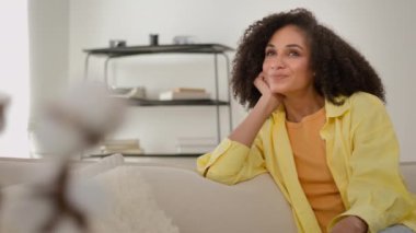 Hayalperest Afrikalı, etnik, sakin bir kadın kanepe üzerinde rüya görüyor rahat bir kız evsahibi rahatça dinleniyor kiralık dairede temiz hava alıyor ve gülümsüyor ve gelecekle ilgili hayaller kuruyor.