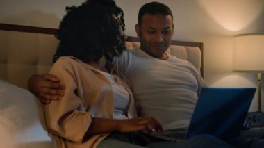Mutlu aile babası, kadın ve erkek arkadaş ve erkek arkadaş Afrika kökenli Amerikalı çift gece evde dizüstü bilgisayarla alışveriş yapıyorlar internetten mal alıyorlar, sohbet ediyorlar bilgisayar kullanarak tartışıyorlar.