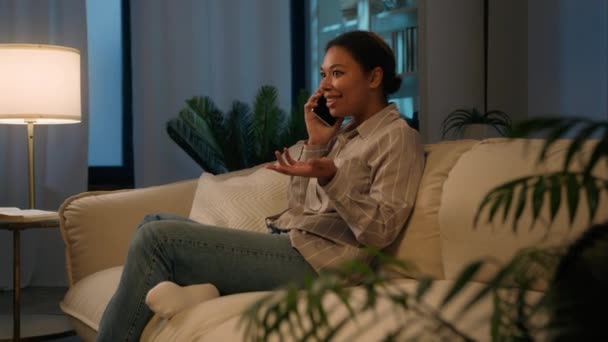 ハッピー アフリカ系アメリカ人 笑顔の女性 夜に携帯電話を話す ケアフリー フレンドリーな携帯電話の会話注文 食べ物 ソファで良いニュースを共有 笑う答え 夜の家で — ストック動画