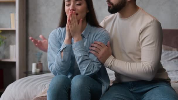 コーカサス カップル ベッドルームでの家族の関係の喧嘩 夫は紛争の後で女性が涙を落ち着かせていることを謝罪する 彼氏は許しの謝罪を求める 感情的な妻は泣く不満を訴える — ストック動画