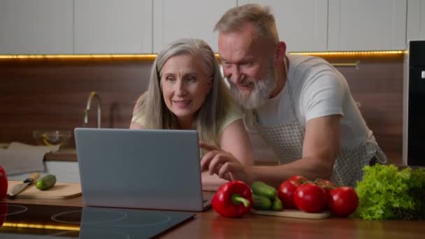 高齢の古いコーカサスカップルファミリーラップトップとキッチンで話す 製品を購入する オンライン食品配達 中年女性と男性のショッピング 一緒にコンピュータで面白いビデオを見る — ストック動画