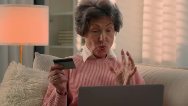 快乐的老年白种人老年女性兴奋的兴奋的退休老年女性在家里沙发网上购物 用笔记本电脑庆祝成功付款网上银行亲吻银行卡 — 图库视频影像