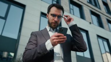Düşünceli iş adamı, yetişkin, açık havada şüpheli beyaz adam akıllı telefon uygulaması e-ticaret online sohbet ile çalışan cep telefonu işveren erkek girişimci CEO 'su kullanıyor.