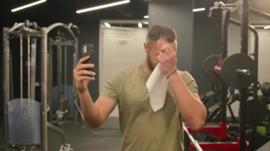 Spor yaptıktan sonra gülümseyen mutlu Afrikalı Amerikalı adam cep telefonu konferansından sonra spor antrenörü sporcu boksörü havluyla terli boksör beden eğitimi blogunda geziniyor.