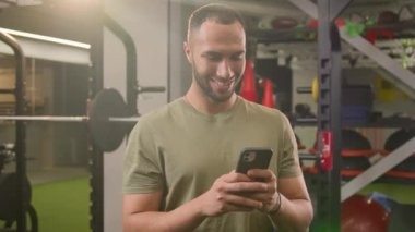 Gülümseyen mutlu Afrikalı Amerikalı sporcu sporcu sporcu spor eğitmeni beden eğitimi eğitmeni gülümseyen, cep telefonlu sosyal medyada gezinen kameralı akıllı telefon uygulamasına bakan, sohbet eden sporcu.