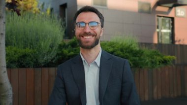 Şehirde gülümseyen başarılı bir işadamı ofis yakınında gözlüklü mutlu bir beyaz adam. Erkek CEO, girişimci, mimar yatırımcı, yatırımcı, açık hava üniversitesi kampüsü profesörü.