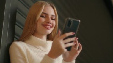 Gülümseyen Kafkasyalı kadın iş kadını İnternet 'e göz atıyor cep telefonuyla mesajlaşıyor mutlu kız akıllı telefon kullanarak video indiriyor sosyal ağlarda geziniyor genç nesil z ve modern teknoloji