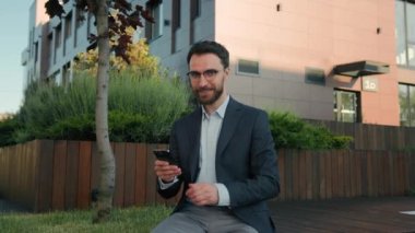 Kafkas mutlu, başarılı işadamı cep telefonuyla mesajlar yolluyor gülümseyen iş adamı girişimcisi akıllı telefon uygulaması kullanıyor sosyal ağ taraması açık havada başparmak hareketi gösteriyor