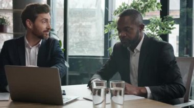 Ofis şirketinde dizüstü bilgisayarı olan iki farklı iş adamı ve Afrikalı Amerikalı iş adamı online sonuç stratejisi pazarlama planlarını tartışıyor.