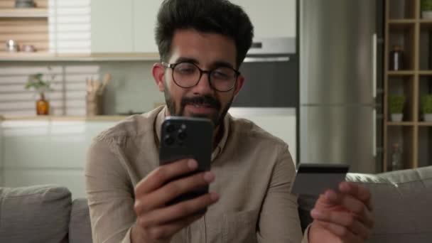 笑顔のアラビアのインドの民族男性買い物客クライアント キッチンでオンラインショッピング モバイルストアアプリで携帯電話の支払い 銀行クレジットカードの購入 商品の注文送金電子商取引 — ストック動画