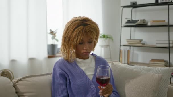 아프리카계 미국인 펜시브 외로운 여성은 테이블에 유리를 와인과 소파에서 — 비디오