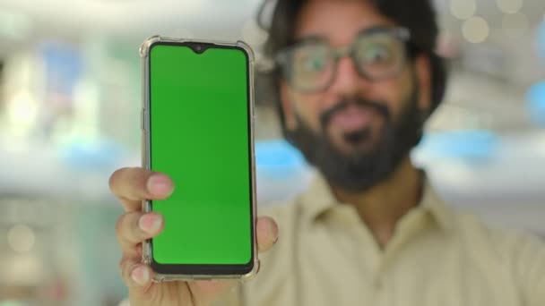 スマートフォンのインドの男性アラビアのビジネスマンを示す緑色のスクリーンのぼやけ男と携帯電話に焦点を当てる 広告のためのクロマキーディスプレイをモックアップして携帯電話を指す 親指を示す ジェスチャーをお勧めアプリ — ストック動画