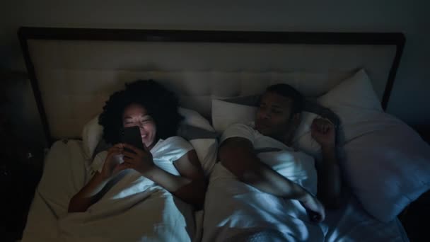 寝室の夜にアフリカ系アメリカ人のカップル家族怒っている男性の夫は ガジェットを使用して大声で笑って妻の女性に怒った — ストック動画