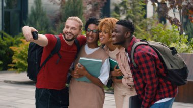 Çok ırklı öğrencilere poz verdirerek mutlu bir gülümseme, çeşitli etnik çeşitlilikteki üniversite kampüsünde öğrenim gördükten sonra cep telefonuna sarılarak selfie fotoğrafı çektirmek.