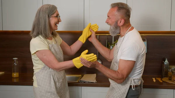 Retired family Caucasian couple washing dishes at home mid age older man and woman enjoying talking do household chores in kitchen dancing husband help wife with tidy clean playful housework fun laugh