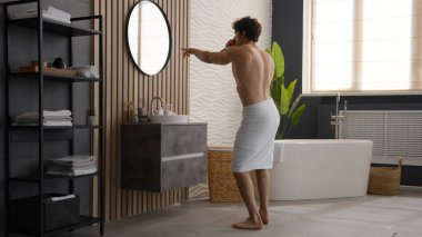 Aktif, esprili, esprili, neşeli, mutlu, neşeli adam. Banyoda havluyla dans eden, kalçasında dans eden, aynaya bakan, saç fırçasında şarkı söyleyen, sabah eğlenen, şapşal erkek.