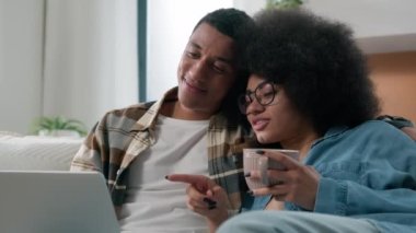 Mutlu çift, Afrikalı, Amerikalı, aile babası, karı koca, sevgili, sevgili, kanepede rahat rahat çay izleyip, bilgisayar kullanarak bilgisayar başında alışveriş yapıyorlar.