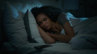 Afro-Amerikan uykusu tükenmiş uyuyan kadın. Gece yarısı yatak odasında uyuyan kız. Cep telefonundan, akıllı telefon ışığından memnun olmayan bir mesaj alıyor.