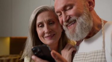 Mutfakta gülen mutlu, yaşlı, beyaz bir aile. Komik mobil uygulama kullanarak olgun çiftleri kaynaştırıyor. Haberleri okuyor, emekli koca ve kadın alışverişini telefonda yapıyor.