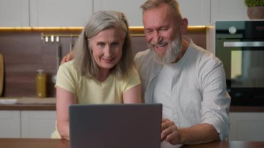 Orta yaşlı aile sohbeti mutfakta dizüstü bilgisayar kullanarak sosyal ağlara göz gezdirip internet üzerinden yemek alışverişi yapıyor beyaz adam ve kadın yeni ürünler satın alıyor bilgisayarlı yaşlı çift.