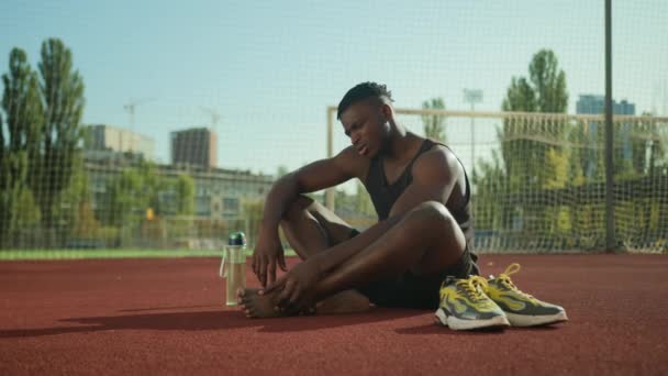 アフリカ系アメリカ人男性ランナーアスリートスポーツマンは トラックアウトトトレーニングを実行するスタジアムでジョギングトレーニングを実行した後 損傷した足のスポーツトラウマに痛みを伴う痛みを伴う呼び出しに苦しんでいます — ストック動画
