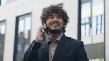 Yakın tebessüm eden Hintli erkek Arap, Latin asıllı, mutlu, etnik, iş adamı, iş adamı, şehirde iş adamı, profesyonel, akıllı telefonlardan konuşan, cep telefonu gülümseyen, dışarıda çalışan işveren.