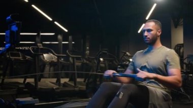 Spor salonu spor kulübünde güçlü ağır sıklet spor aletleri antrenmanı güçlü Afrikalı Amerikalı sporcu yatay çekiş bloğu egzersizi yapıyor.