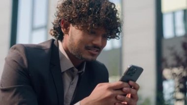 Şehirdeki Hintli işadamı etnik adam iş uzmanı gülümseyen mutlu Arap erkek girişimci cep telefonuyla sohbet ediyor akıllı telefon sosyal medya uygulaması ile cep telefonu ile iletişim kuruyor