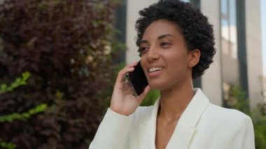 Şehir merkezine giderken mutlu bir şekilde gülümseyen Afro-Amerikan kadın işkadını iş kadını iş adamı arkadaşça görüşmeler yapan iş kadını şehir içinde cep telefonuyla konuşuyor.