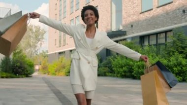 Afro-Amerikan mutlu kadın butik dükkanından şehre geliyor dans eden kız müşteri müşterisi müşteriler dışarı çıkıyor alışveriş torbaları indirimli dans ediyor.
