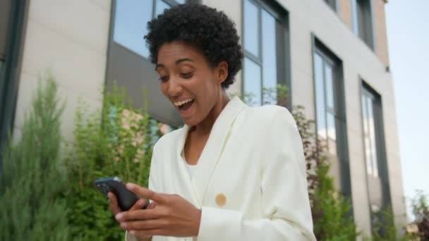 アフリカ系アメリカ人の幸せな少女は街の外で歩く女性を興奮させる民族のビジネスマンは 携帯電話で勝利の勝利のビジネスの成功を達成し スマートフォンの勝利で良いニュースを読みます — ストック動画
