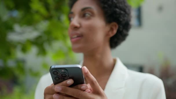 笑顔のアフリカ系アメリカ人女性ビジネスチャット ソーシャルメディアモバイルアプリのテキストネットワーク待機タクシーの注文 離れて考える屋外の女の子 公園のスマートフォンを持つ都市女性の携帯電話を使用して — ストック動画