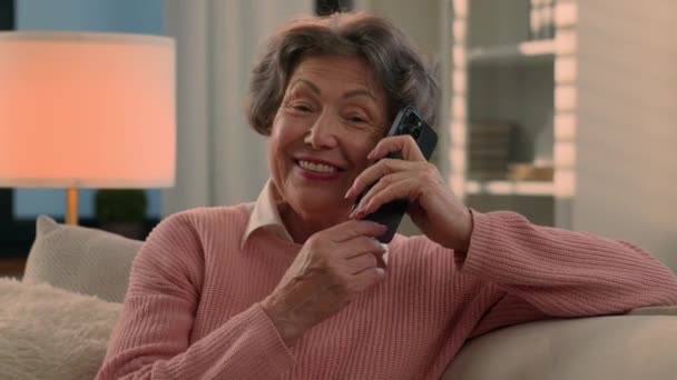 快乐地笑着交谈电话白种人老太太无忧无虑的老太太听着有趣的新闻笑着退休老奶奶手机在家里的交流 — 图库视频影像