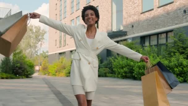 アフリカ系アメリカ人幸せな女性 ブティックショップから街を歩く 踊る買い物客 女性バイヤー 外に出る顧客 ダンス ショッピングバッグの購入割引で回転 — ストック動画