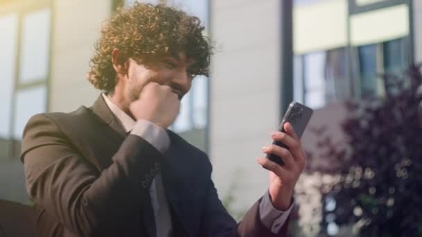 西班牙裔喜形于色的微笑兴奋的阿拉伯男性印度男性惊奇的商人获得了好消息成就的胜利提供了商机商业上的成功获得了男人智能手机在城市里喜出望外的手机 — 图库视频影像