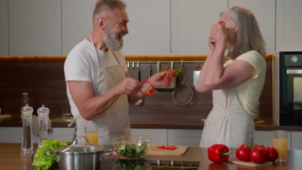 有趣的退休白种人夫妇制作红辣椒眼镜圈 有快乐的中年家庭妇女和爷爷奶奶在厨房里做蔬菜沙拉 和食物鬼混 — 图库视频影像