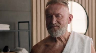 Banyoda, banyoda, mutlu bir portre. Yaşlı, beyaz, yaşlı, yetişkin, beyaz saçlı, yaşlı bir adam. Duştan sonra omuzlarında beyaz havluyla, evde kameraya yakından bakıyor.