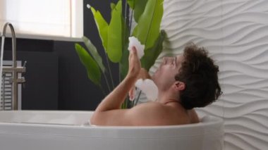 Kafkas gevşemiş sakin adam sıcak banyo oyununda banyo yaparken köpüklü köpüklü köpüklü mutlu erkek kaygısız adam banyoda duş alırken dinleniyor otel tuvaletinde temizlik prosedürü uyguluyor.