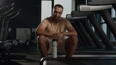 Yorgun Afrikalı Amerikalı sporcu. Spor şişesinden su proteini takviyesi alıyor. Yorgun sporcu dinleniyor. Koşu bandında koştuktan sonra dinleniyor.