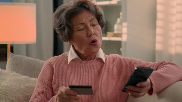 白种人老太婆退休老奶奶老奶奶买家网上购物网上购物用手机和银行卡庆祝高兴地在家里买智能手机 — 图库视频影像