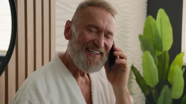白种人退休老人上了年纪六十岁的老年男性养恤金领取人讲手机交谈智能手机友好对话浴室答话叫早间卫生洗澡水交流 — 图库视频影像