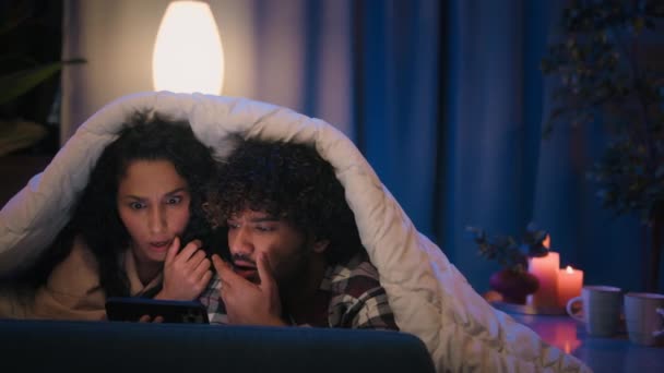 不同的夫妻在夜晚用手机赢得了博彩阅读好男人和女人在家里沙发上获得了成就感快乐的网上赢得了胜利智能手机盖着被子 — 图库视频影像