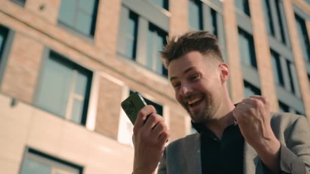 携帯電話にSmsメッセージを受け取る驚くべき幸せな慎重なビジネスマンは オフィスセンターの近くのスマートフォンで成功を祝う喜びの男性の勝利を興奮させた良いニュースを読みます — ストック動画