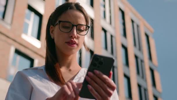 严重困惑的女商人女学生女企业家戴着眼镜在办公室外用手机发短信查看电子邮件阅读社交网络上的新闻思考 — 图库视频影像