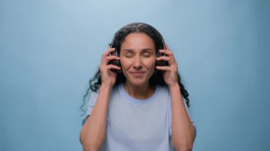 Arap kadın mutlu Müslüman kız kaygısız neşeli bayan kulaklık taktı, dans etti, müzik dinledi, dans etti eğlenceli eğlenceli hareketler yaptı, hareketli mavi arka plan